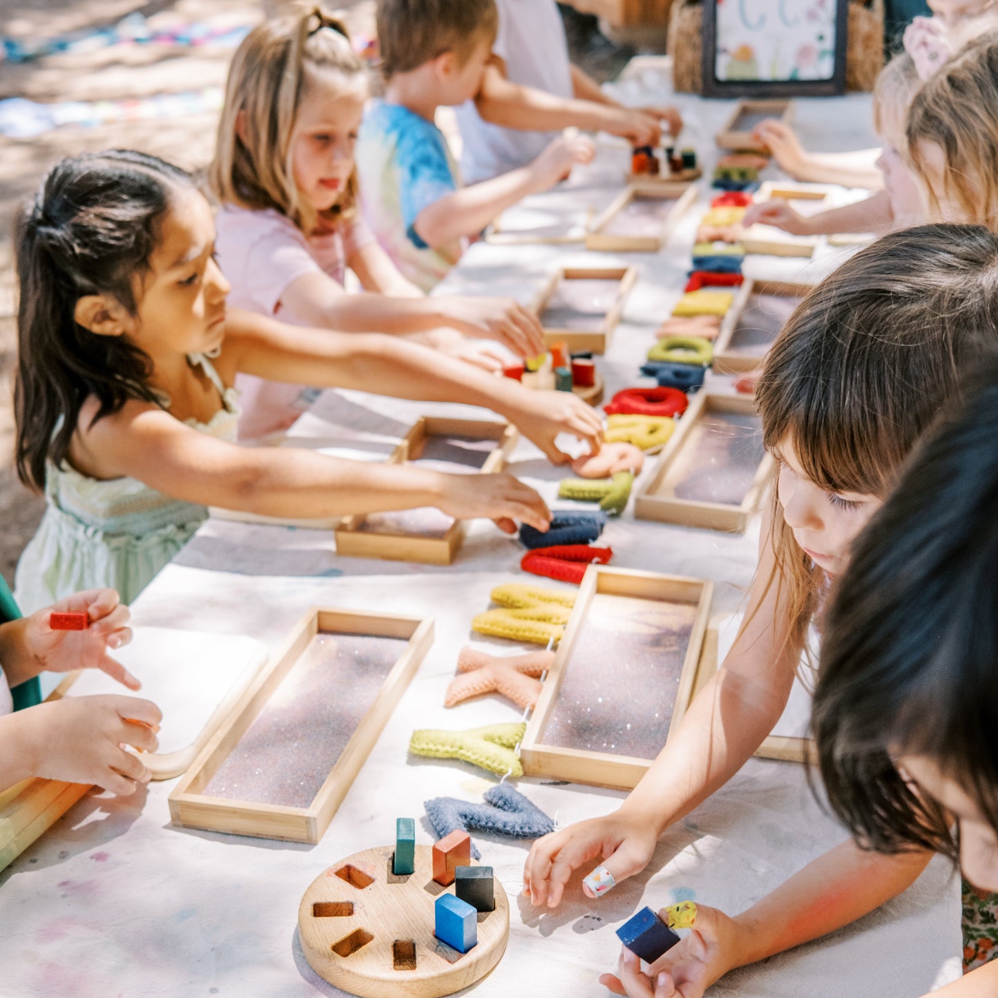 Children playing with educational toys at a long table outdoors.