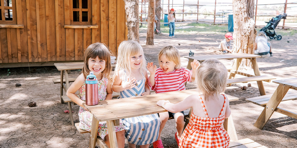 Children smiling at each other on a picnic table