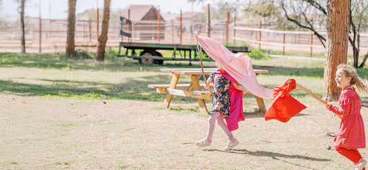 Girls laughing and running with silk flags tied to sticks.