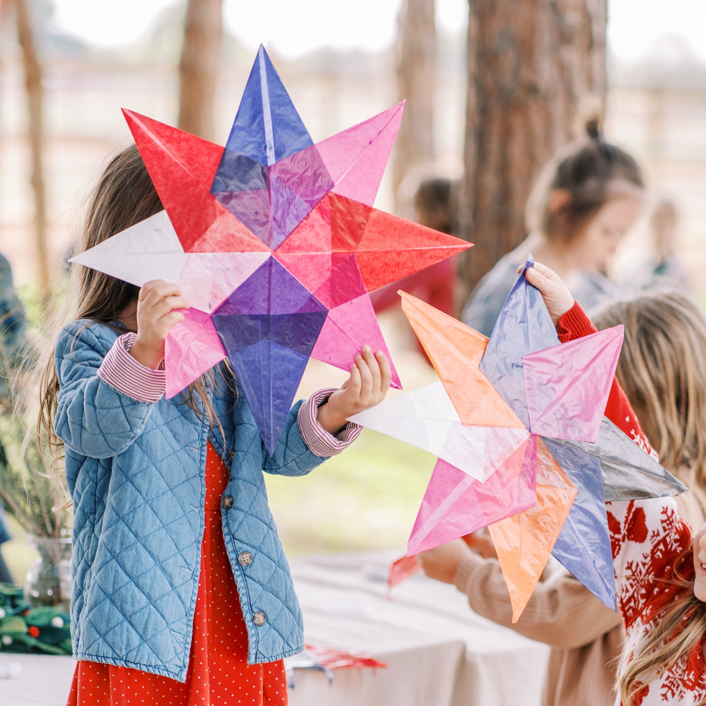 Children holding colorful star-shaped paper crafts outdoors.