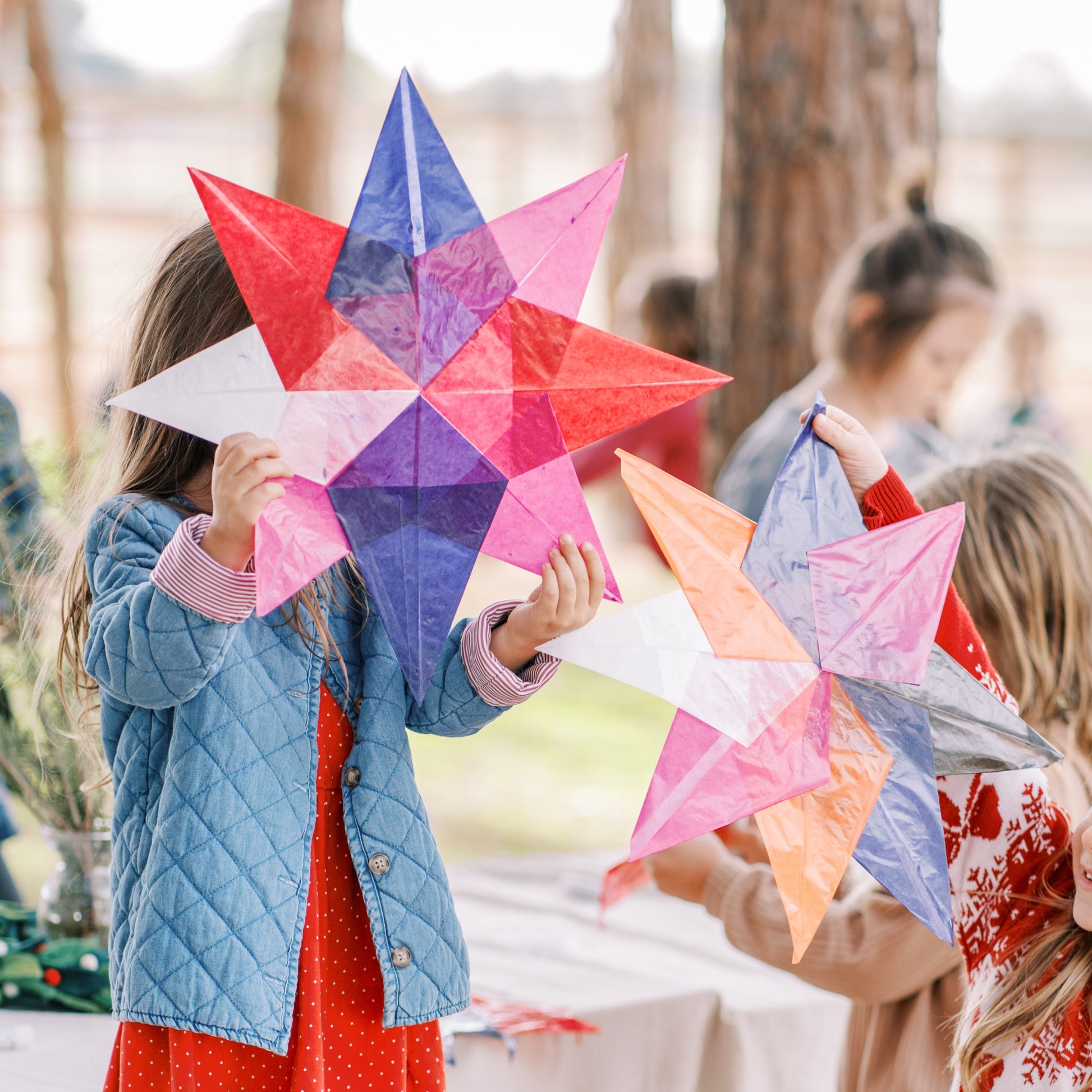 Children holding colorful star-shaped paper crafts outdoors.