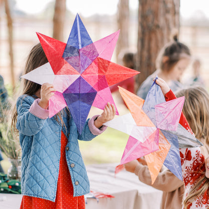 Children holding colorful star-shaped paper crafts outdoors.
