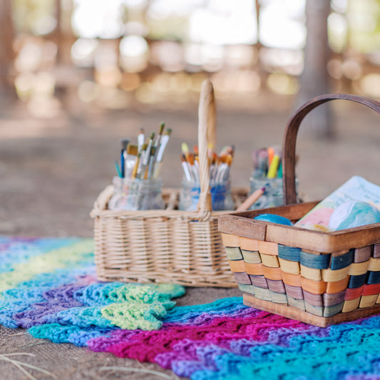 Colorful crocheted blanket with baskets on a wooden surface outdoors.