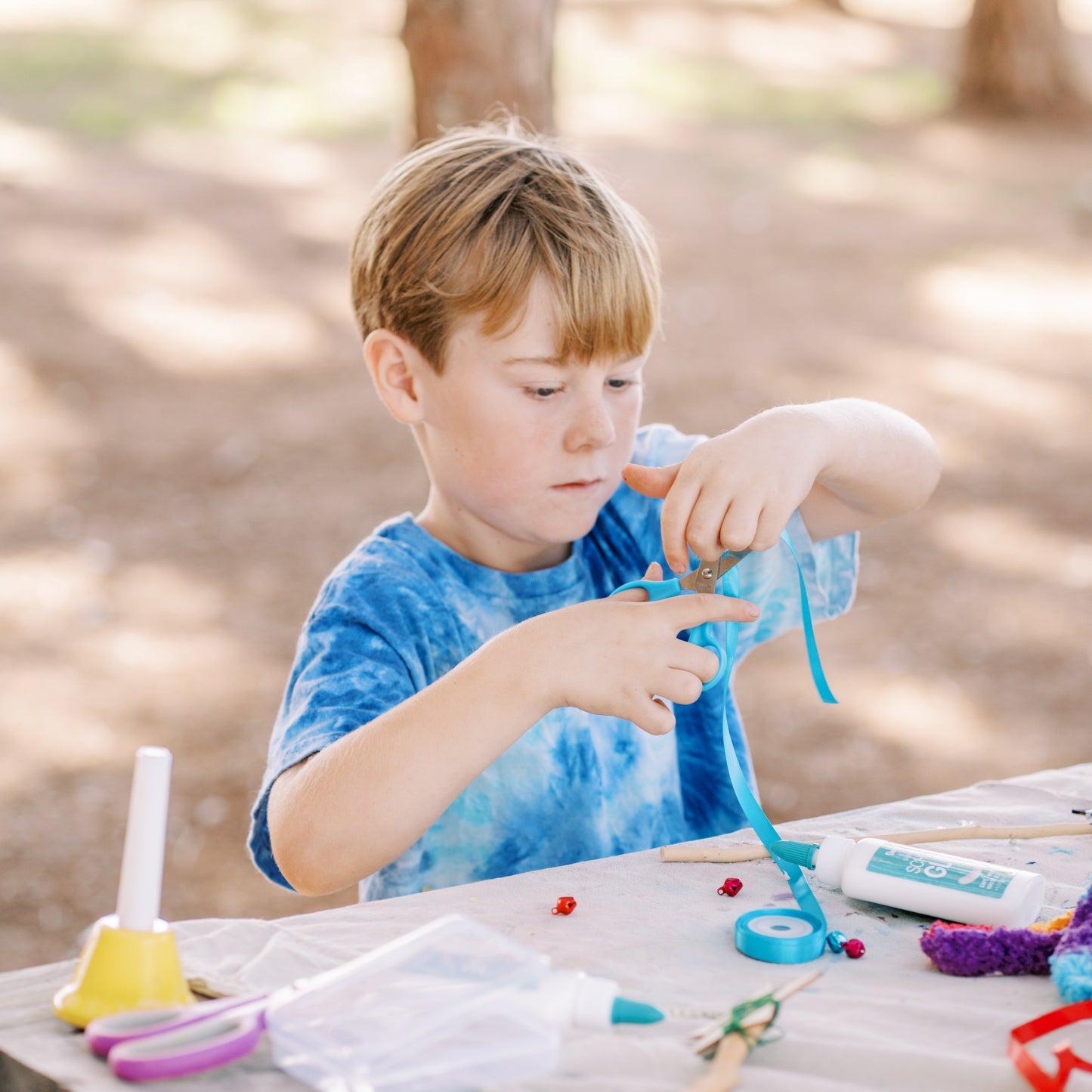 Child crafting outdoors at a wooden table with various supplies.