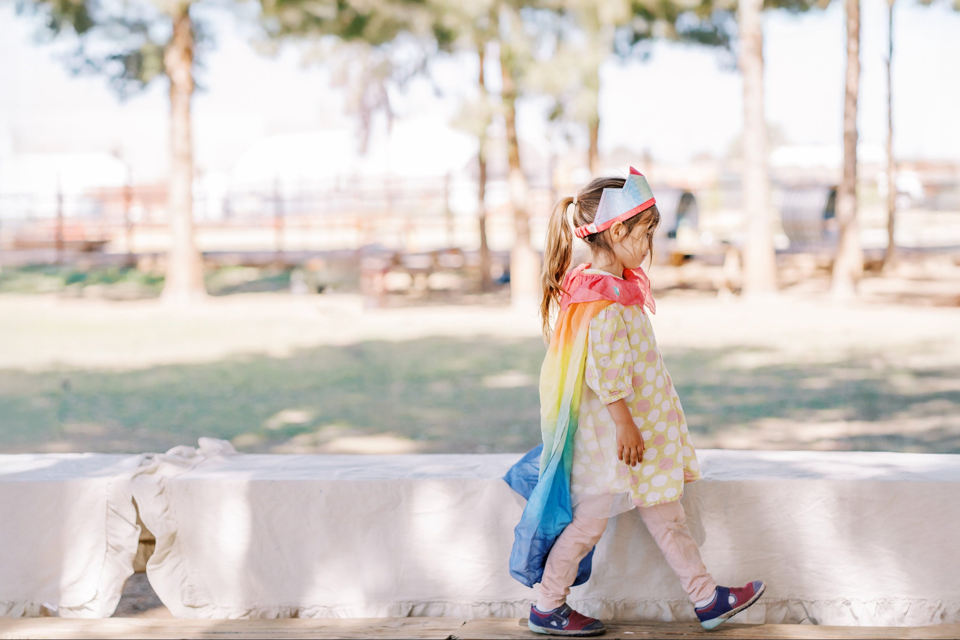 Child in a rainbow dress standing on a ledge with trees in the background