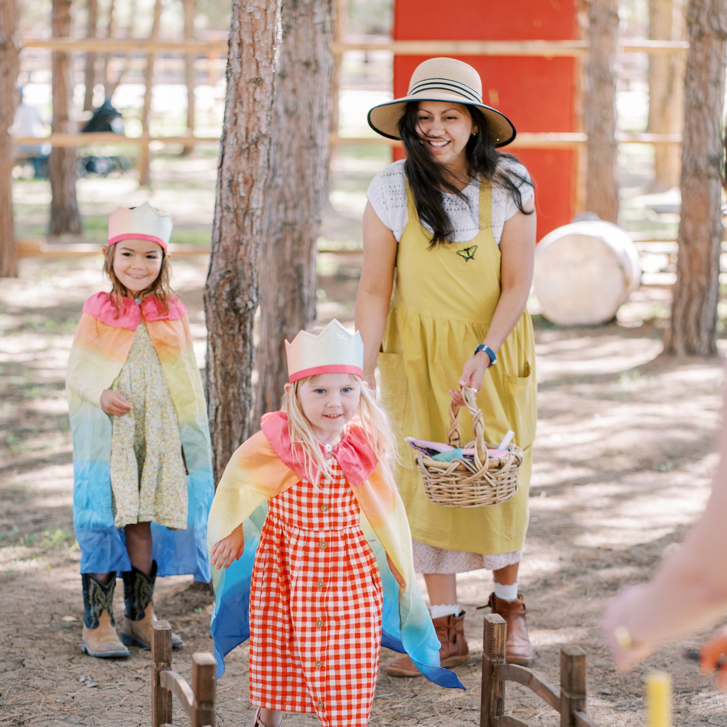 Woman and two children in colorful costumes walking over a wooden bridge in a forest setting.