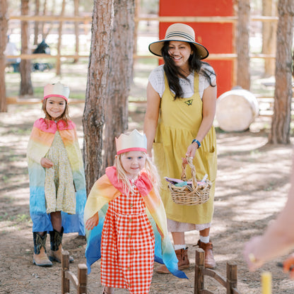 Woman and two children in colorful costumes walking over a wooden bridge in a forest setting.