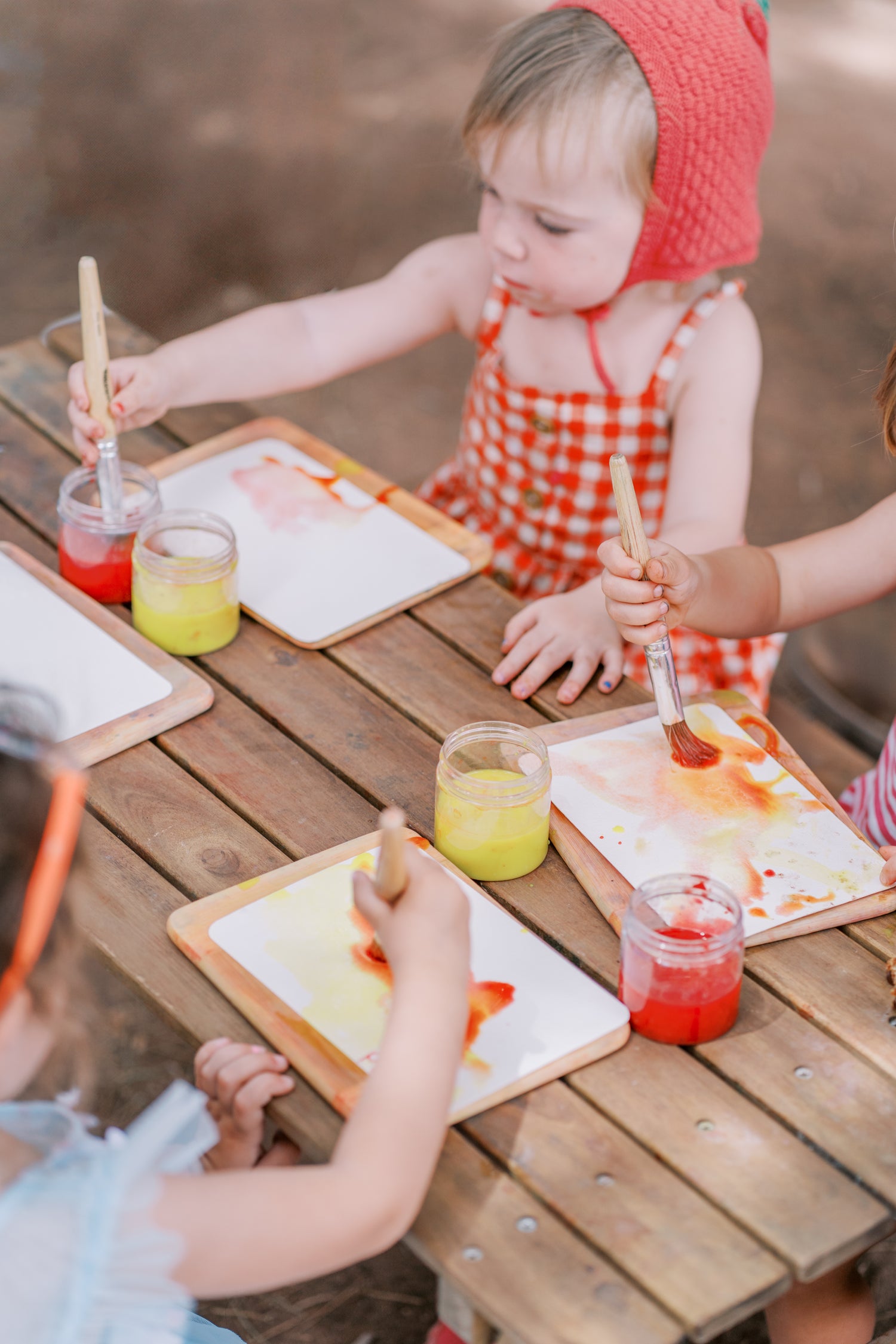 Children painting at a wooden table outdoors