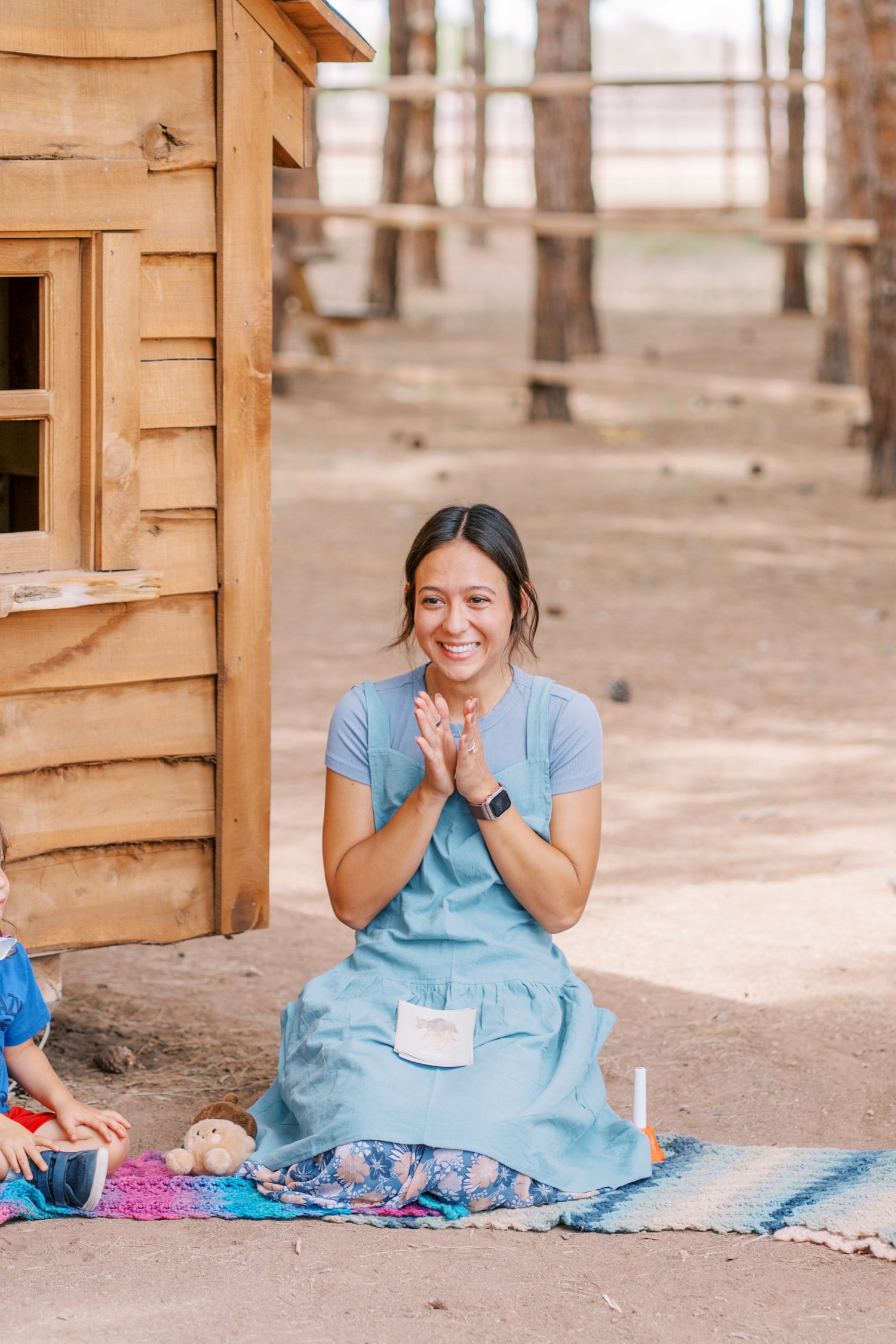 Woman in a blue dress sitting on a blanket in front of a wooden cabin