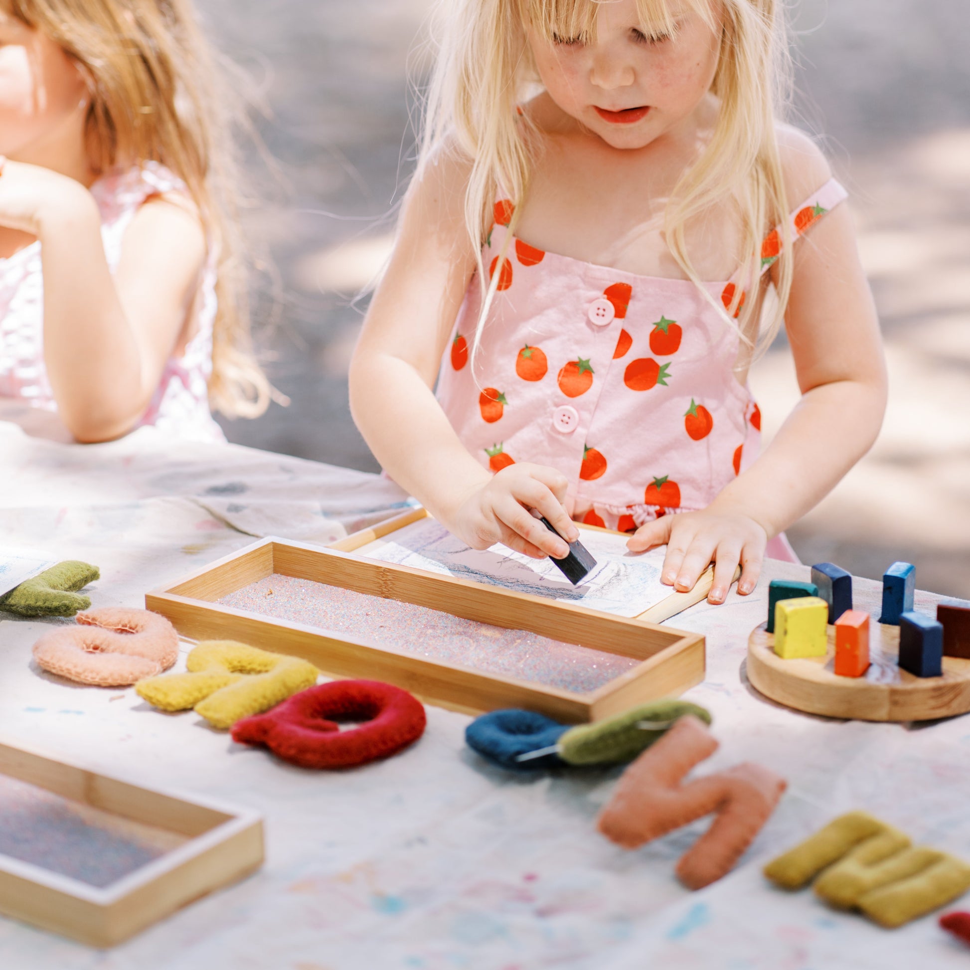 Two young girls playing with educational toys outdoors on a sunny day.