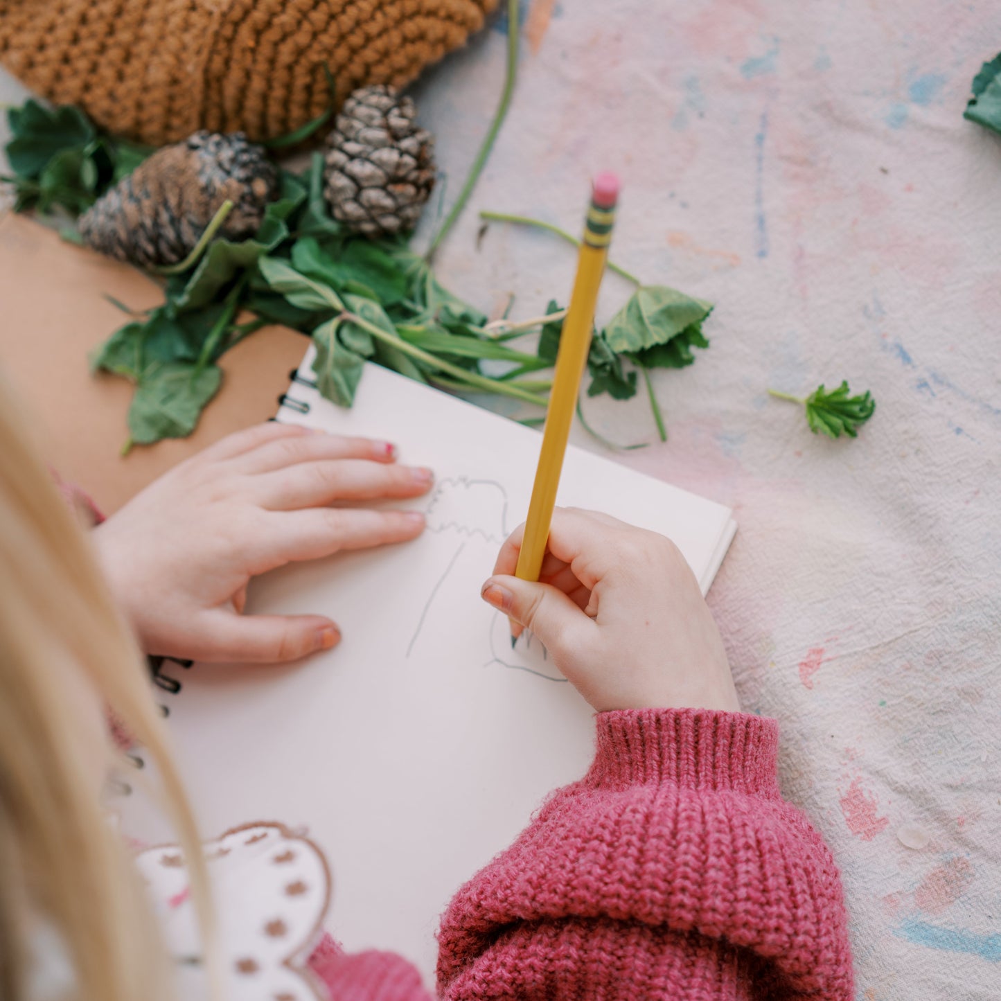 Person in pink sweater holding a pencil over a notebook with nature-themed decor.