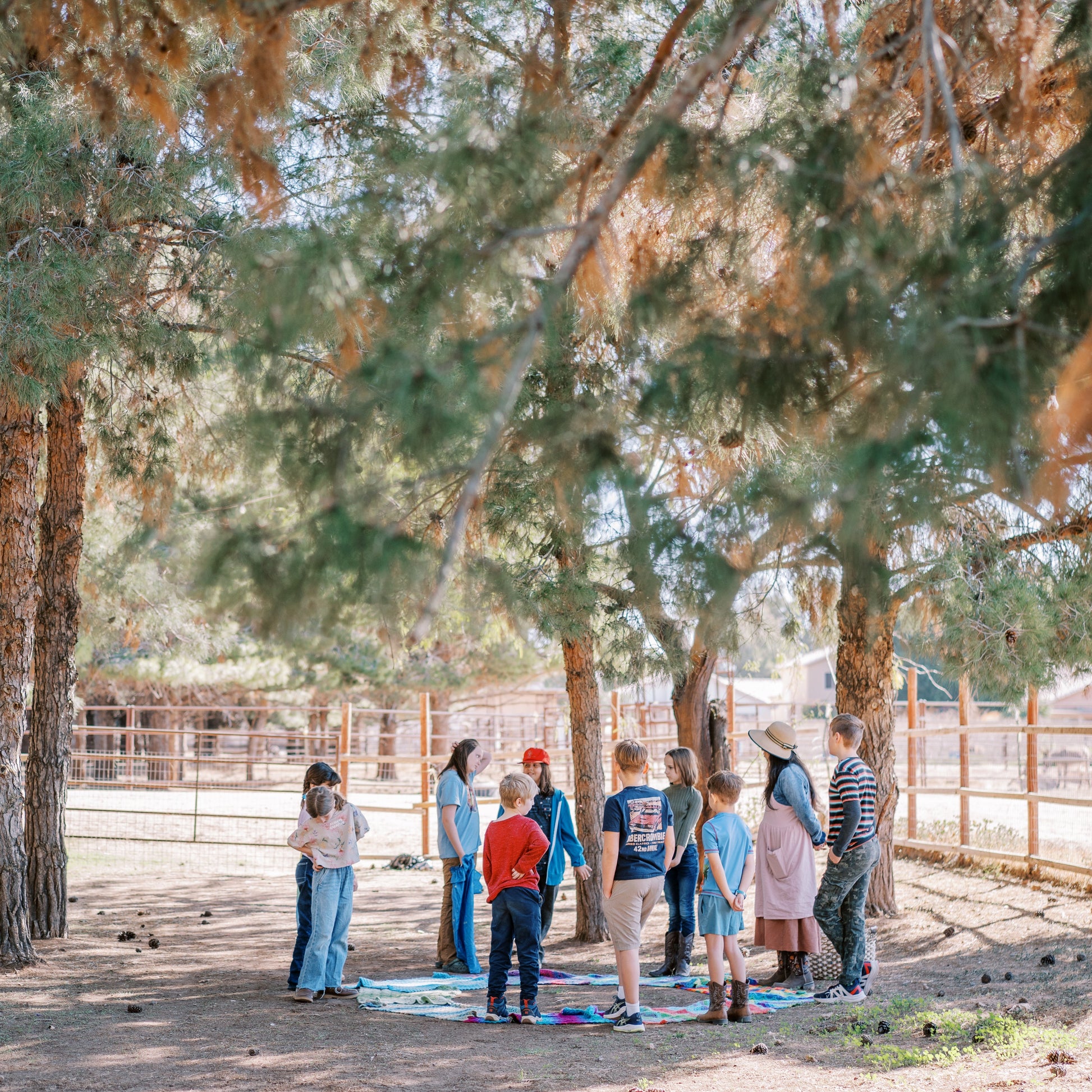 Group of people standing outdoors under trees, possibly in a park or rural area.