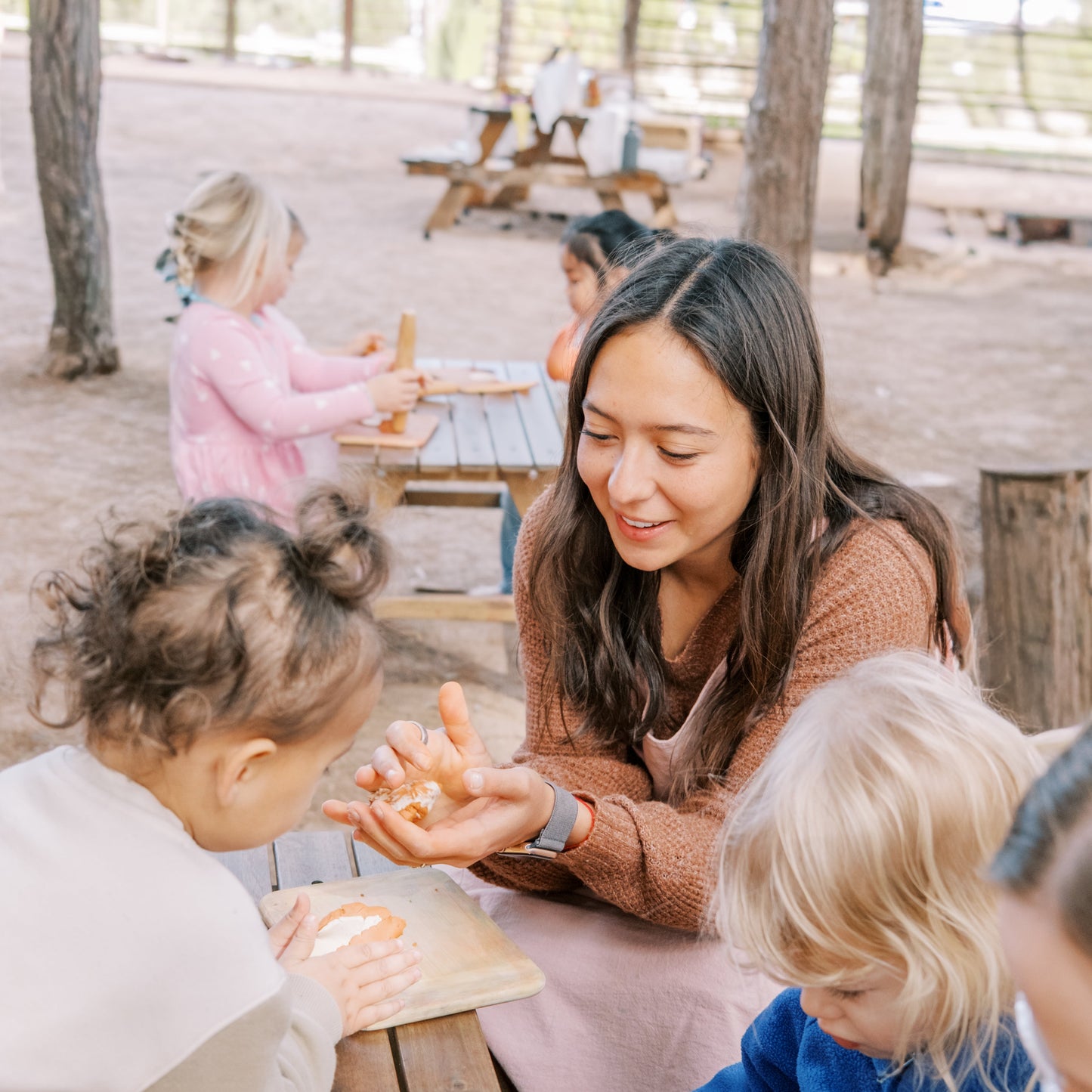 Woman interacting with children at a wooden table outdoors
