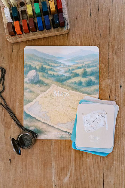 Cards on a table with a compass necklace and crayons.