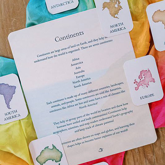 One large card with several smaller cards laying on a rainbow colored silk.