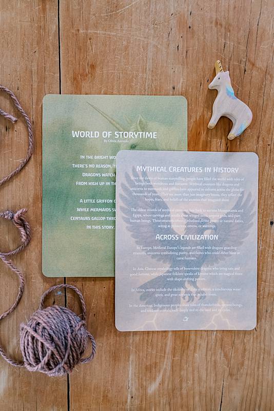Two large cards with a wooden unicorn and a ball of yarn on a table.