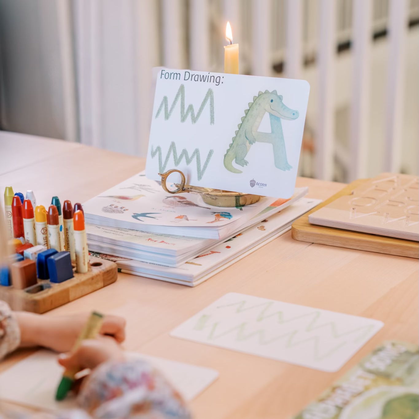 Child drawing with crayons on a table with art supplies and books.