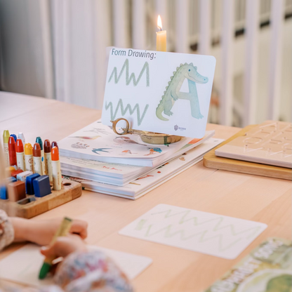 Child drawing with crayons on a table with art supplies and books.