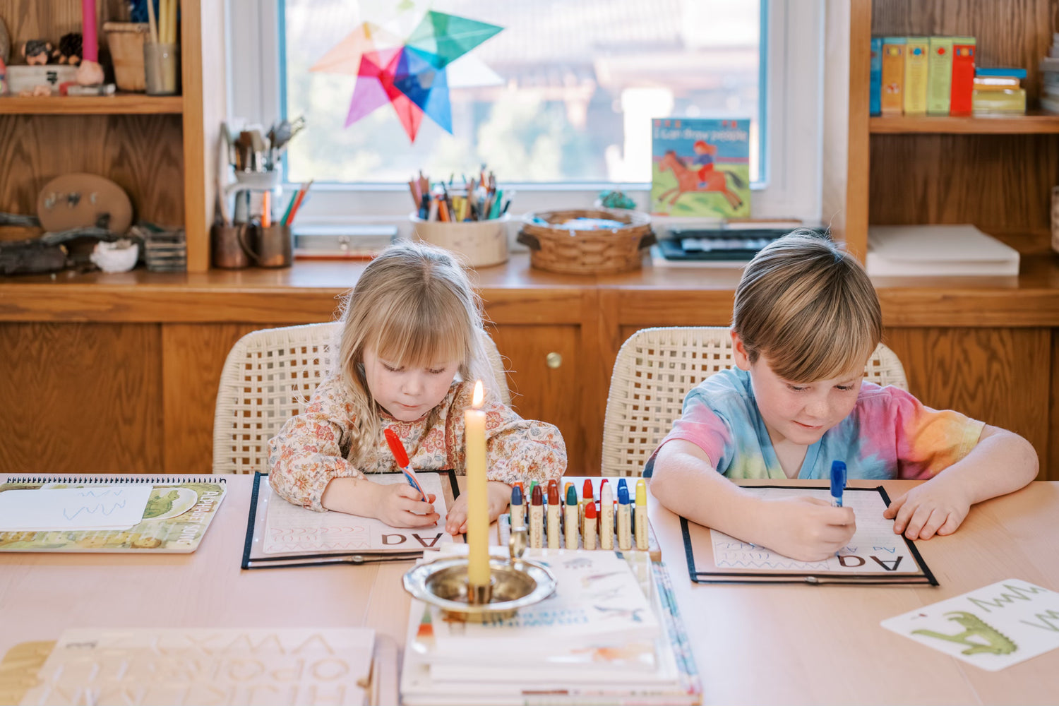 Two children sitting at a table with educational materials and a candle.
