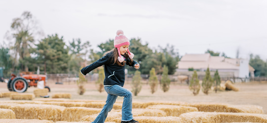 girl jumping across hay bales at a farm