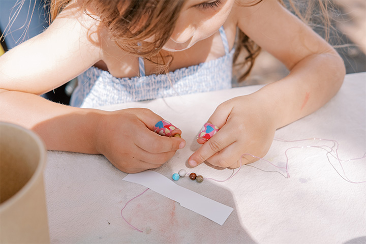 Child crafting a necklace at a picnic table. 