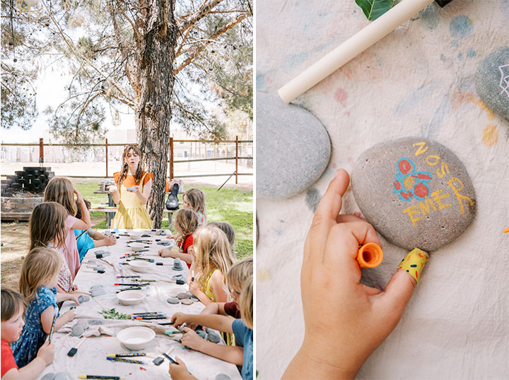 A picnic table full of childrne looking at a teacher and an image of a child's hand holding a rock with paint on it. 