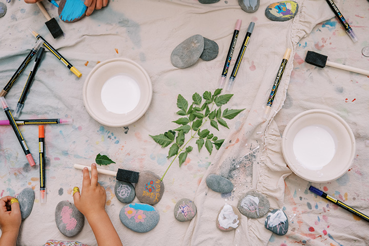 A table with leaves, rocks, and painting supplies along with a child's hand