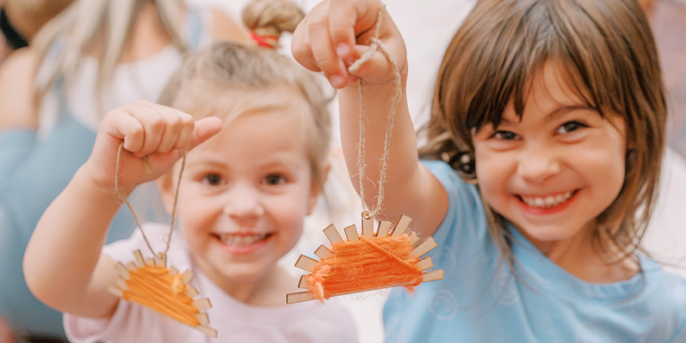 Children holding up crafts to the camera and smiling